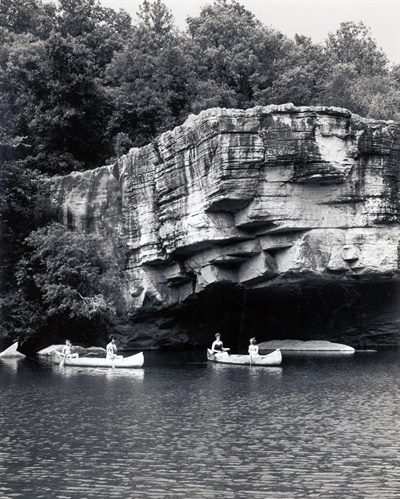floating skull bluff in the state park People in canoes paddling under a large rock overhanging the water.