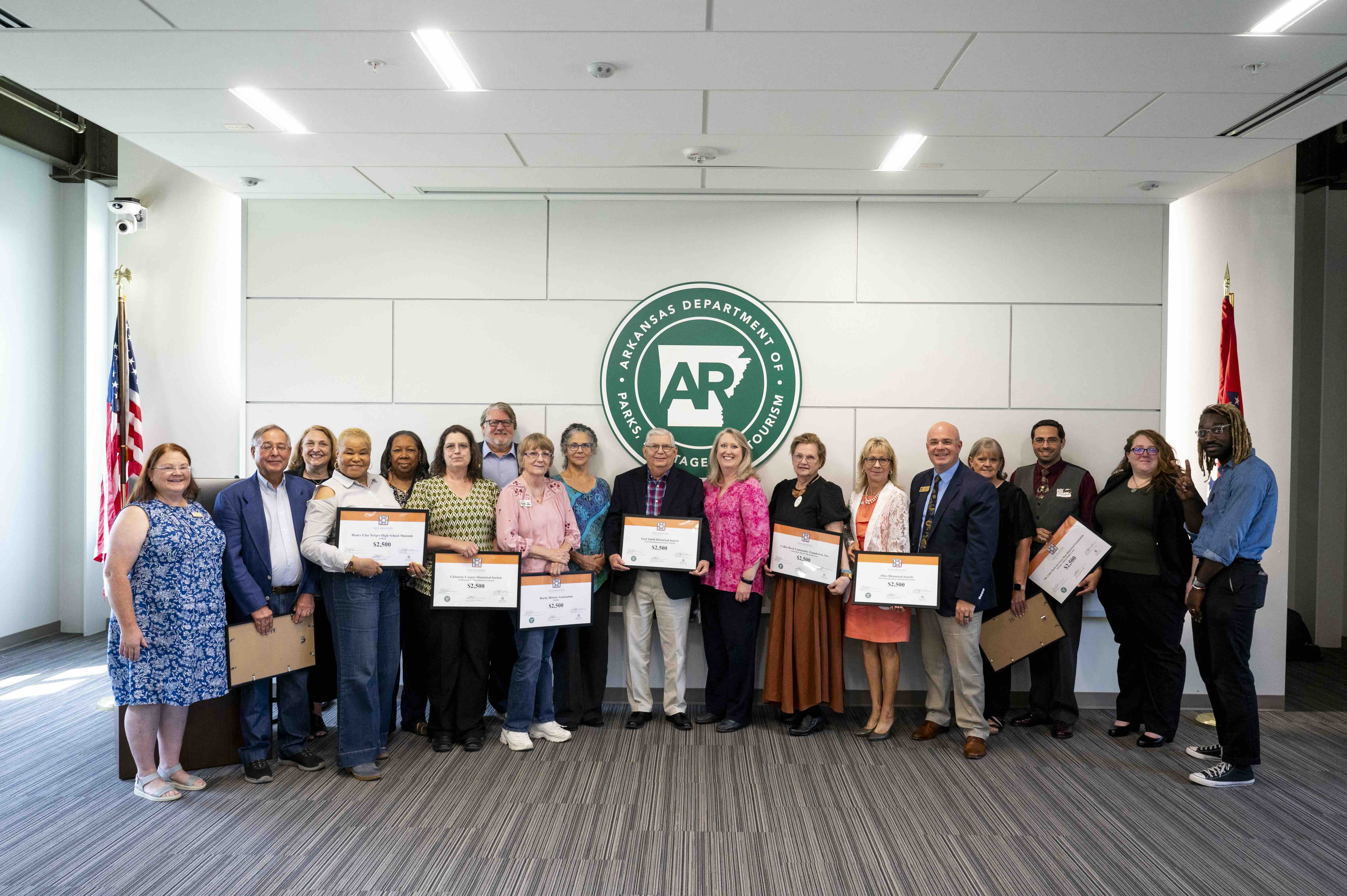A group of grant recipients holding framed certificates posing in front of a large white wall.