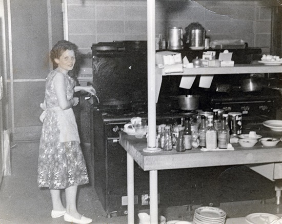 Josephine Dodd in the kitchen at Buffalo River State Park A woman standing next to a large stove and table full of bottles.