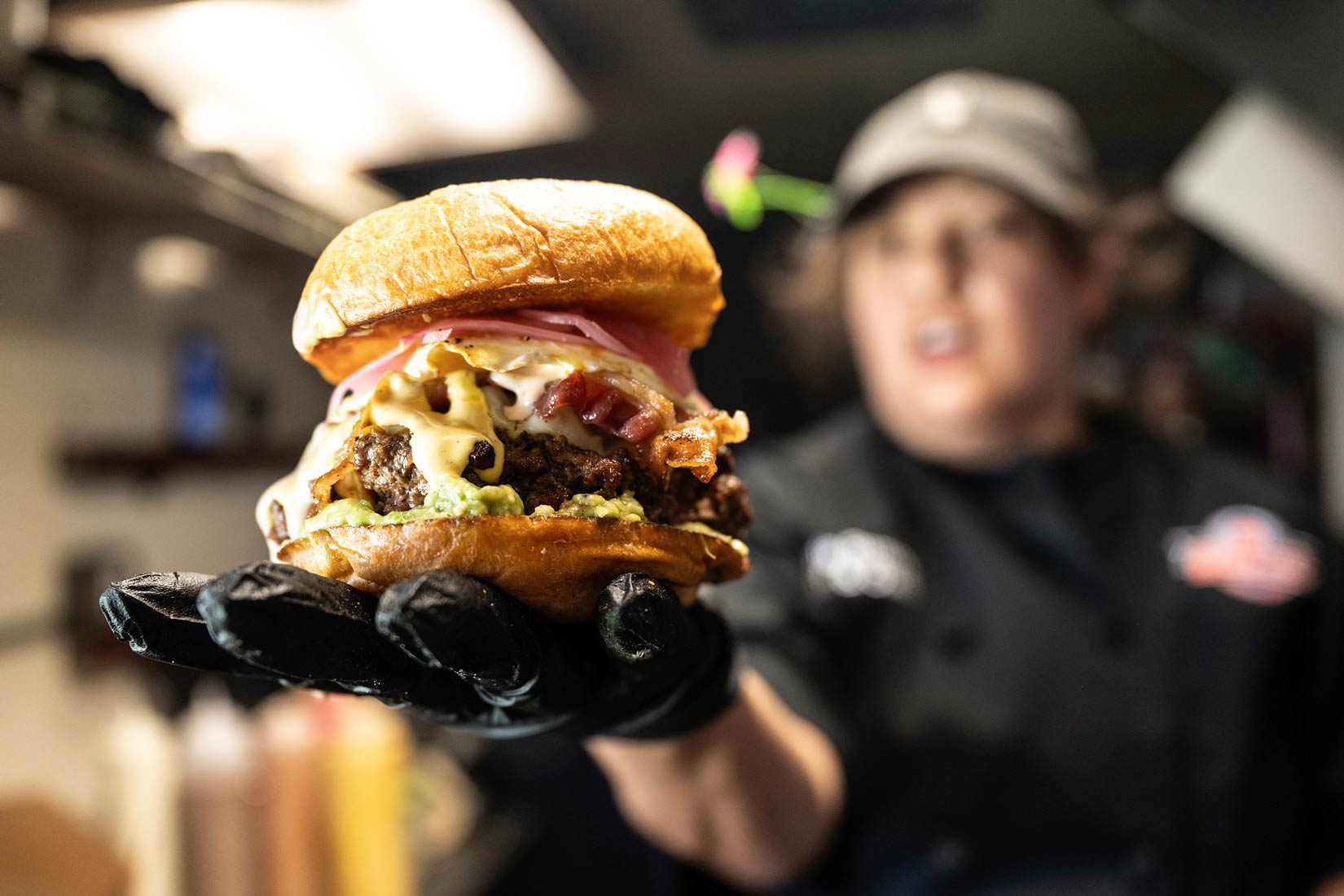 Large cheese burger held in the hand of one of Meme's Burgery owners.